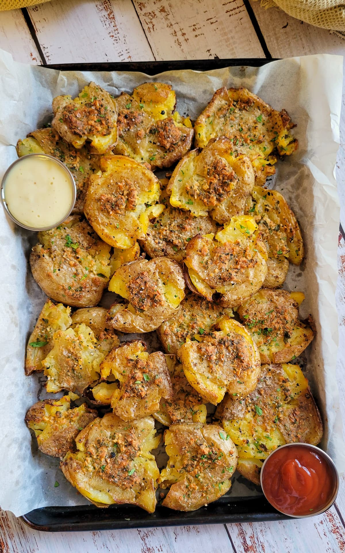 smashed potatoes piled onto a parchment lined baking sheet with 2 dipping sauces