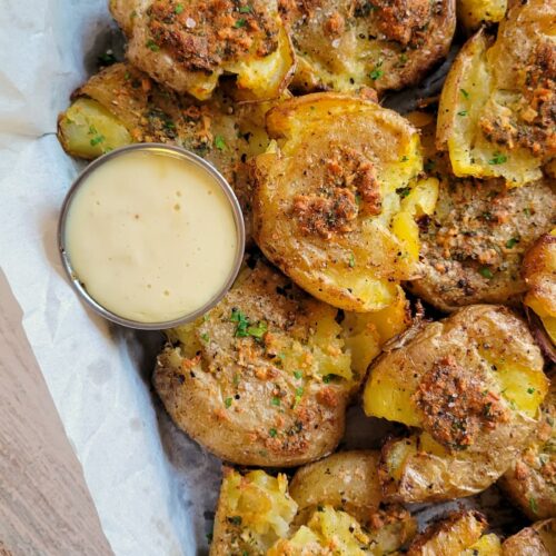 smashed potatoes on a parchment lined baking sheet with a white dipping sauce