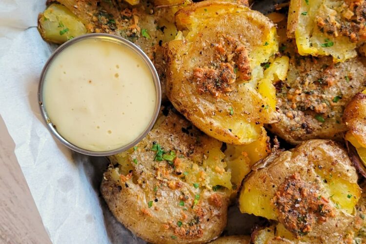 smashed potatoes on a parchment lined baking sheet with a white dipping sauce