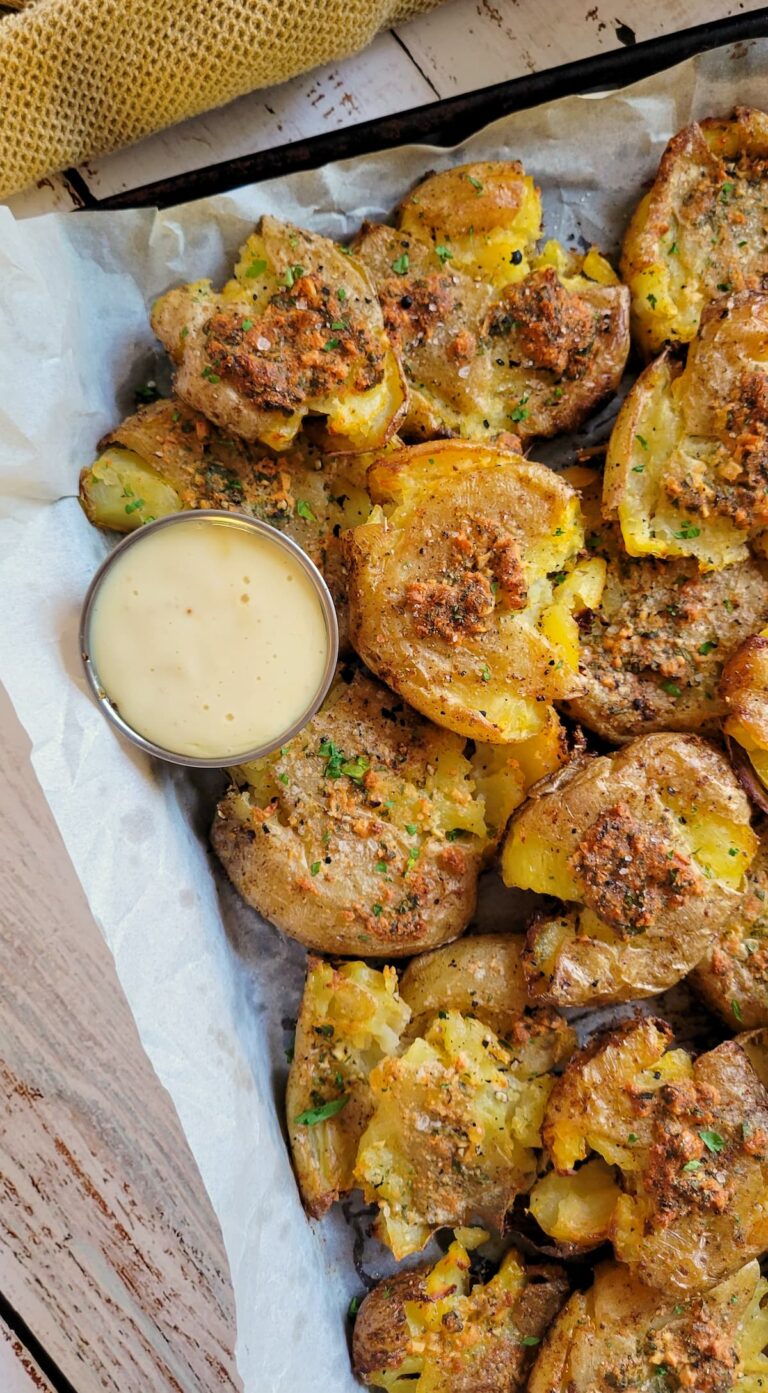 smashed potatoes on a parchment lined baking sheet with a white dipping sauce