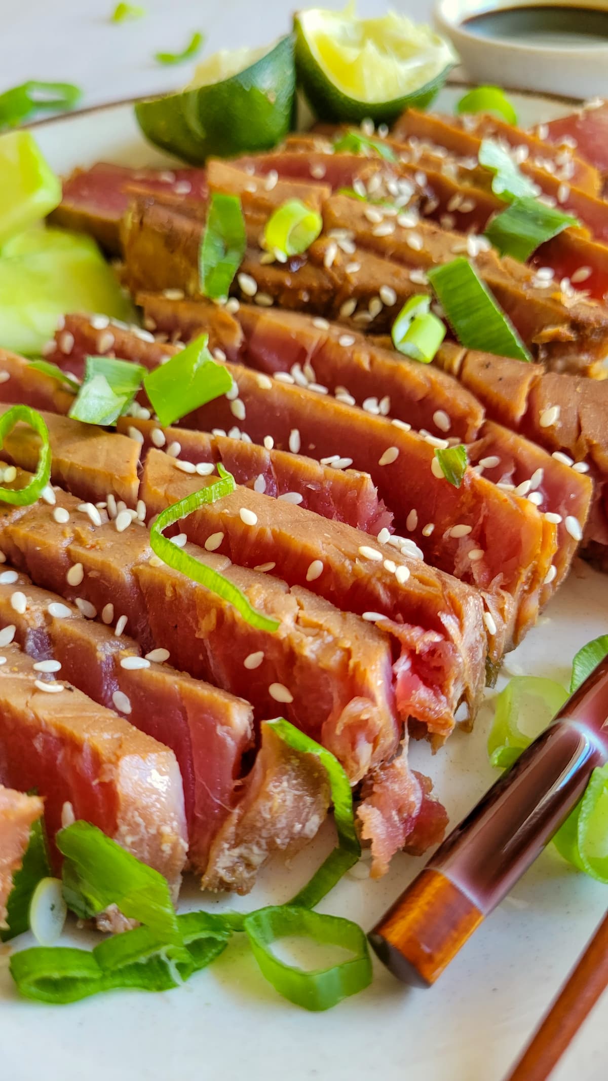 side view of sliced rare tuna steak topped with green onions and sesame seeds, lime in the background