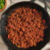 ground beef in a skillet with chopped veggies in bowls surrounding it