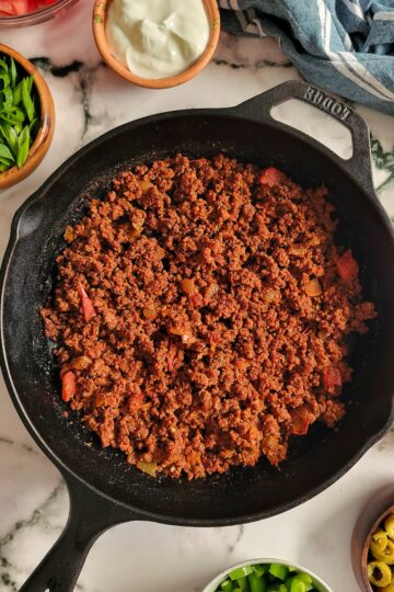 ground beef in a skillet with chopped veggies in bowls surrounding it