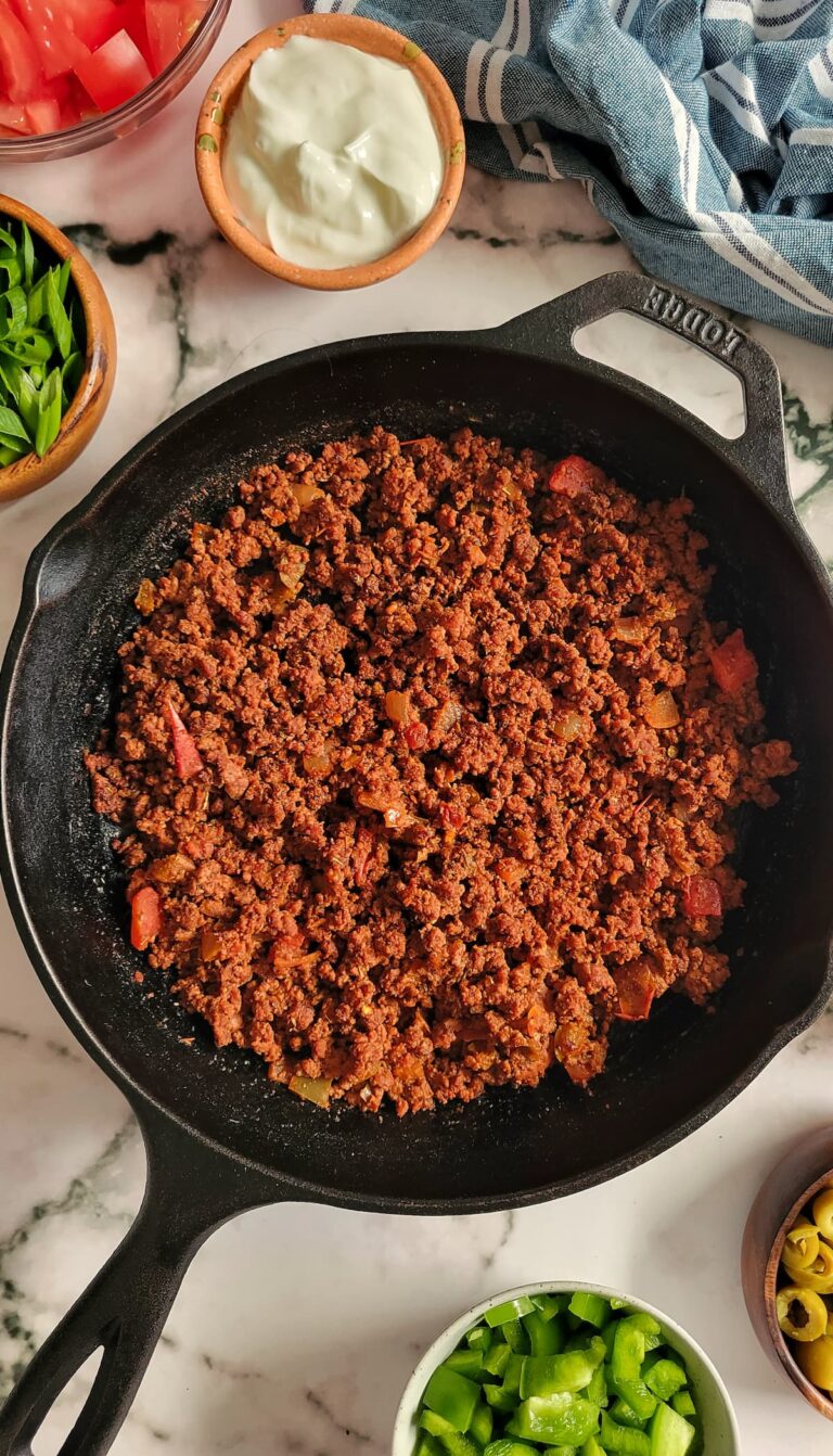 ground beef in a skillet with chopped veggies in bowls surrounding it