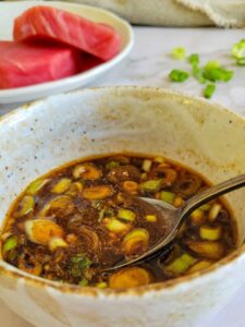 marinade for tuna steak in a bowl with a spoon, 2 tuna steaks in the background