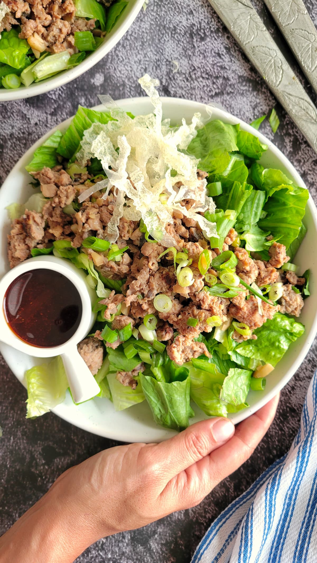 hand holding a large bowl of salad with ground chicken and green onions