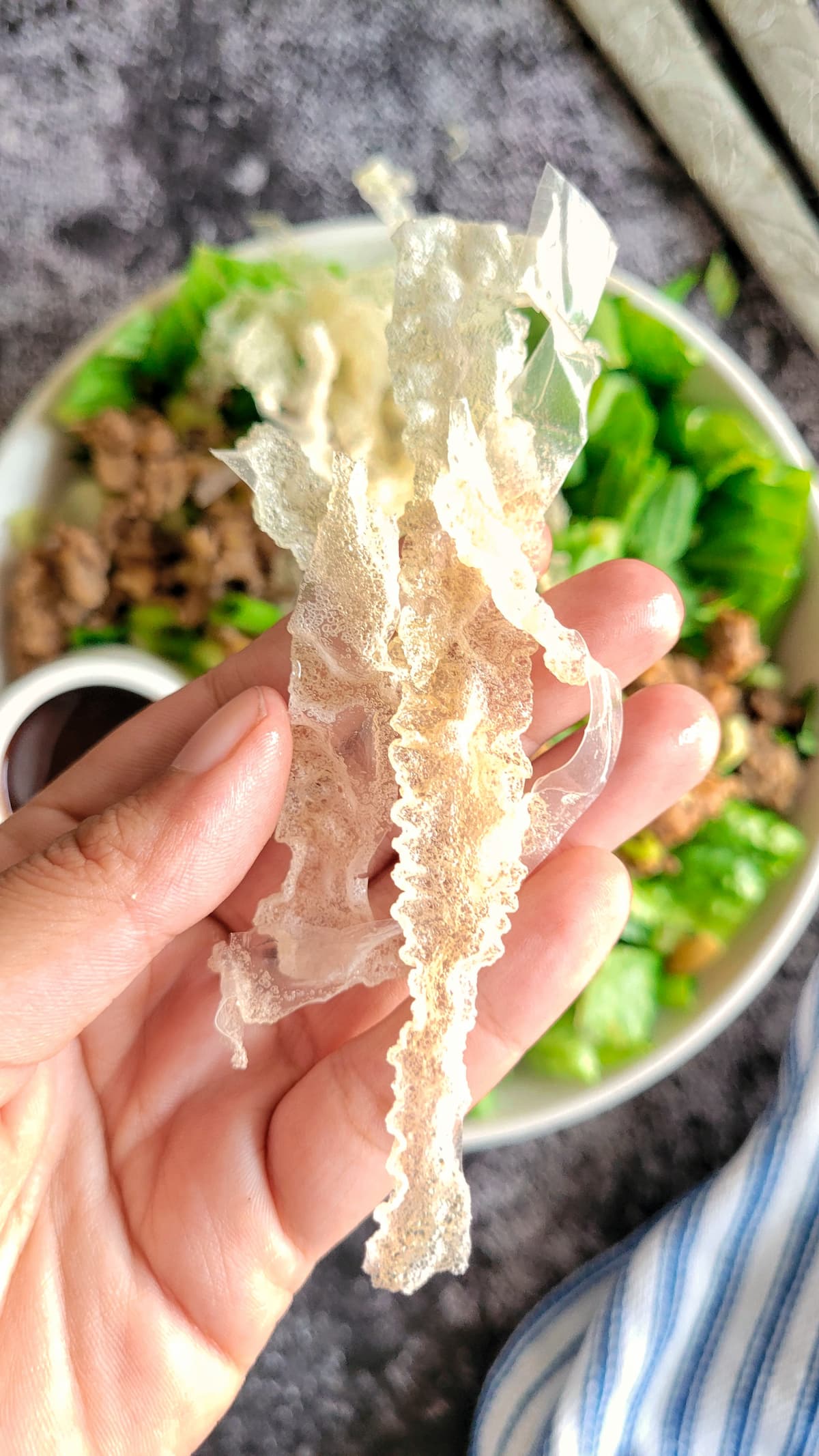hand holding fried rice paper strips over a large bowl of salad