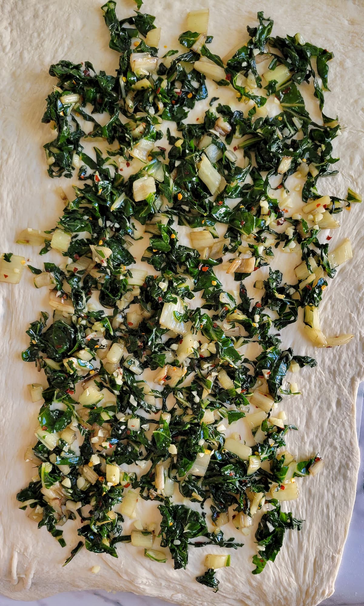 chopped and seasoned swiss chard in rolled out raw dough