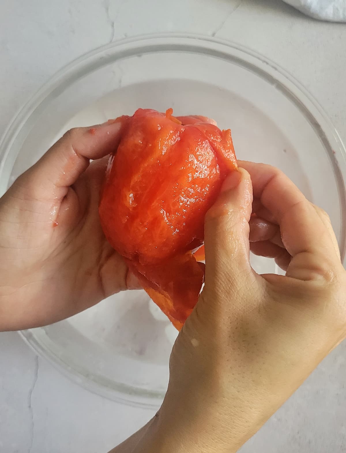 hands peeling the skin off of a whole tomato