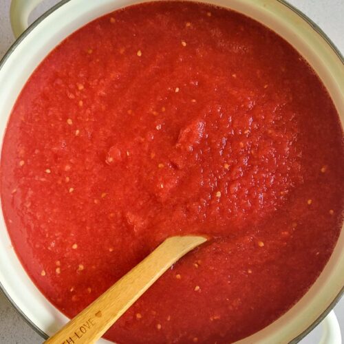 pot of tomato sauce with a wooden spoon in it, garlic and basil in the background