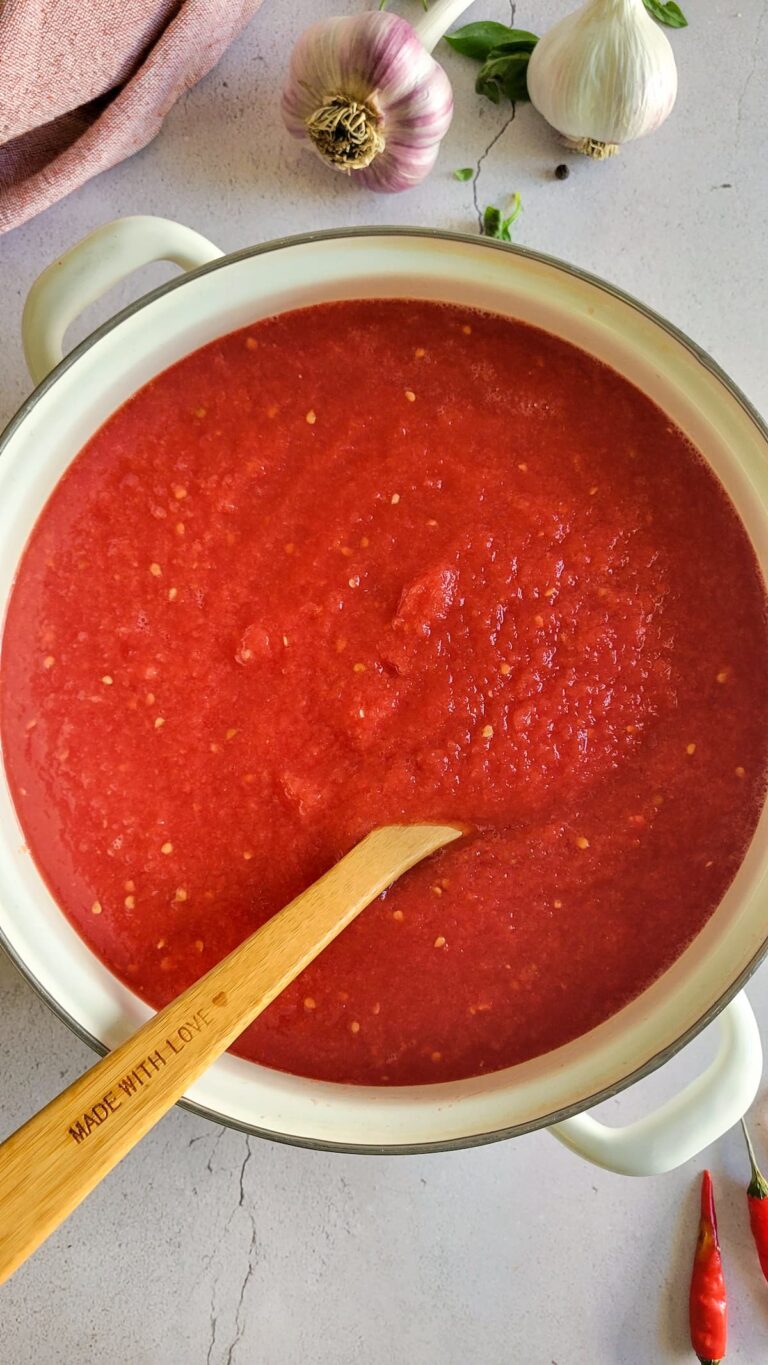 pot of tomato sauce with a wooden spoon in it, garlic and basil in the background