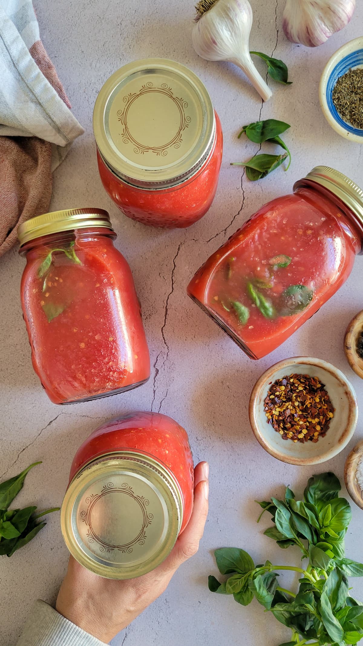 4 jars of homemade tomato sauce next to herbs and spices