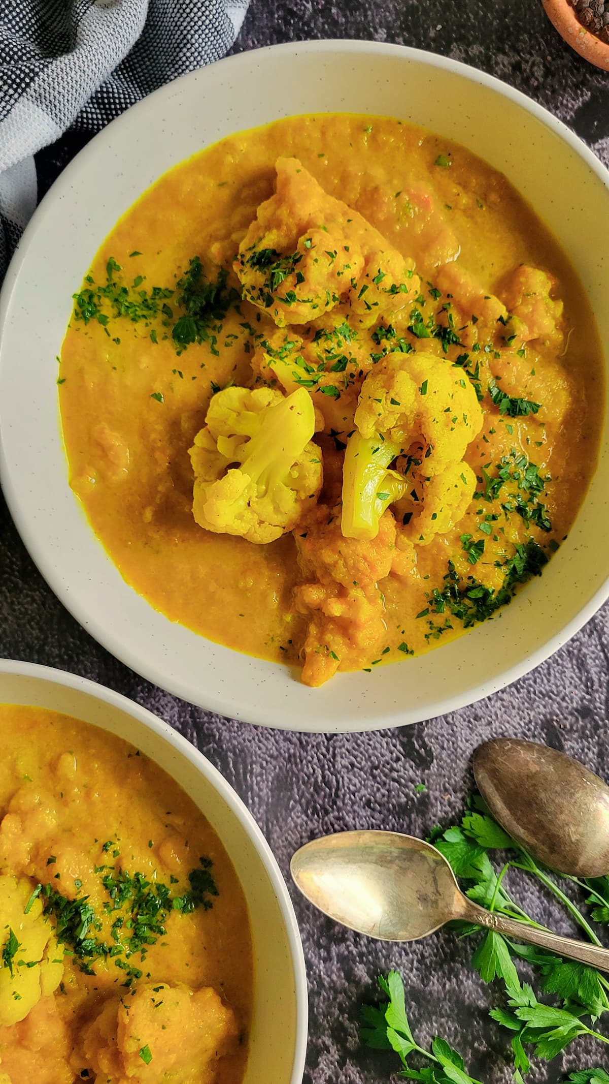 two bowls of bright yellow soup topped with cauliflower florets and chopped fresh parsley