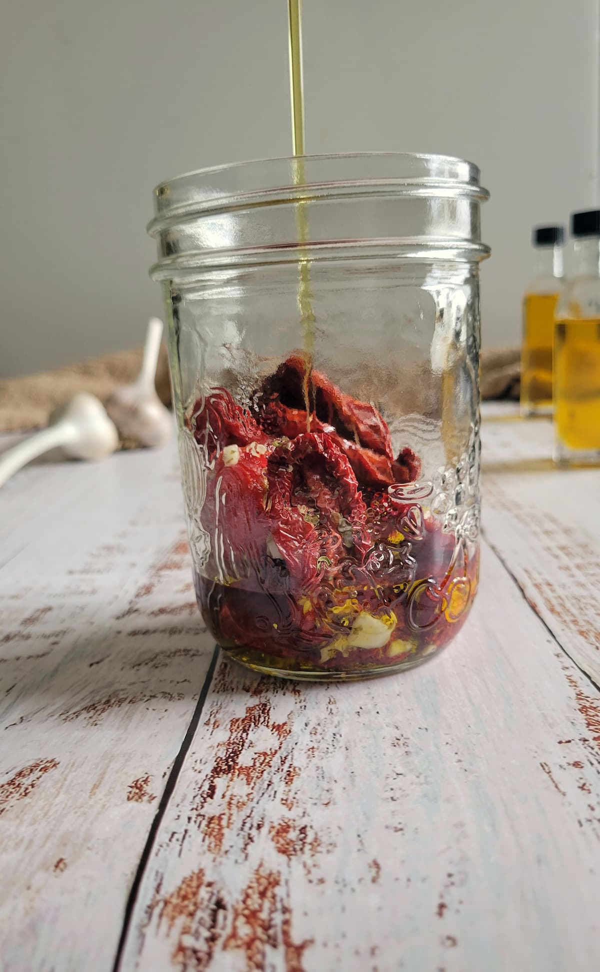 oil being poured into a jar with sun dried tomatoes and garlic