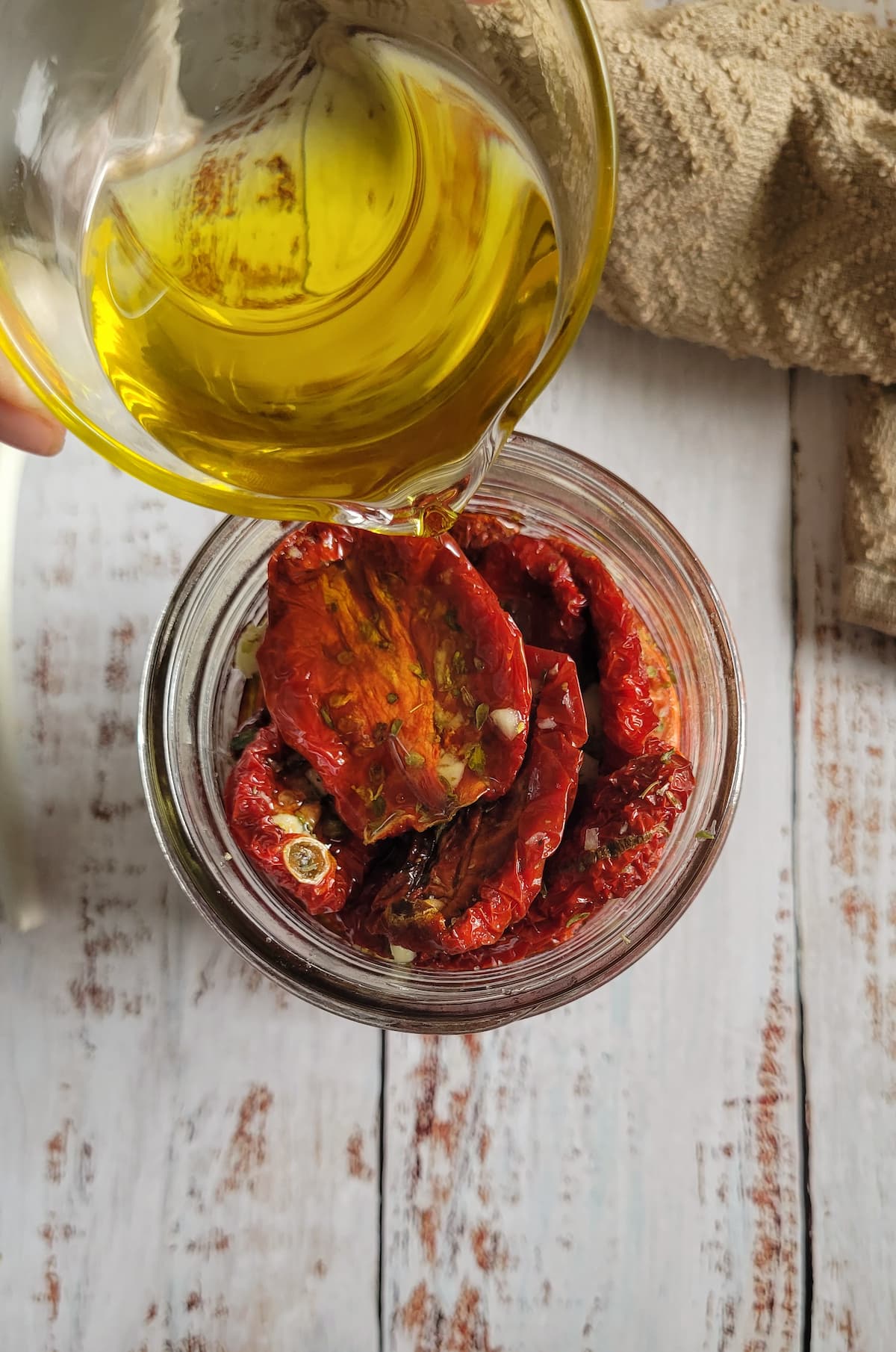 oil being poured into a jar of sun dried tomatoes
