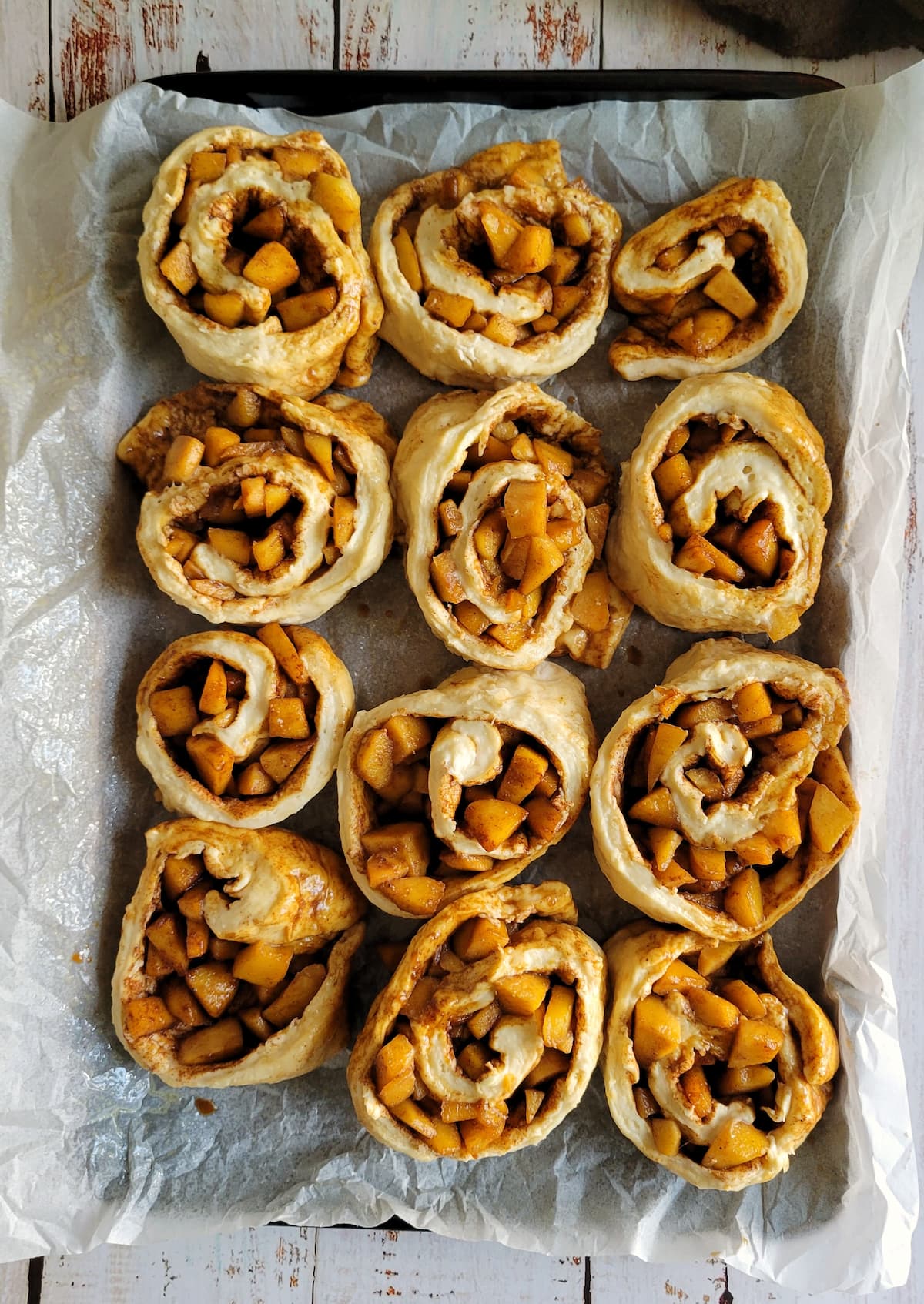 unbaked cinnamon and apple rolls on a parchment lined baking sheet