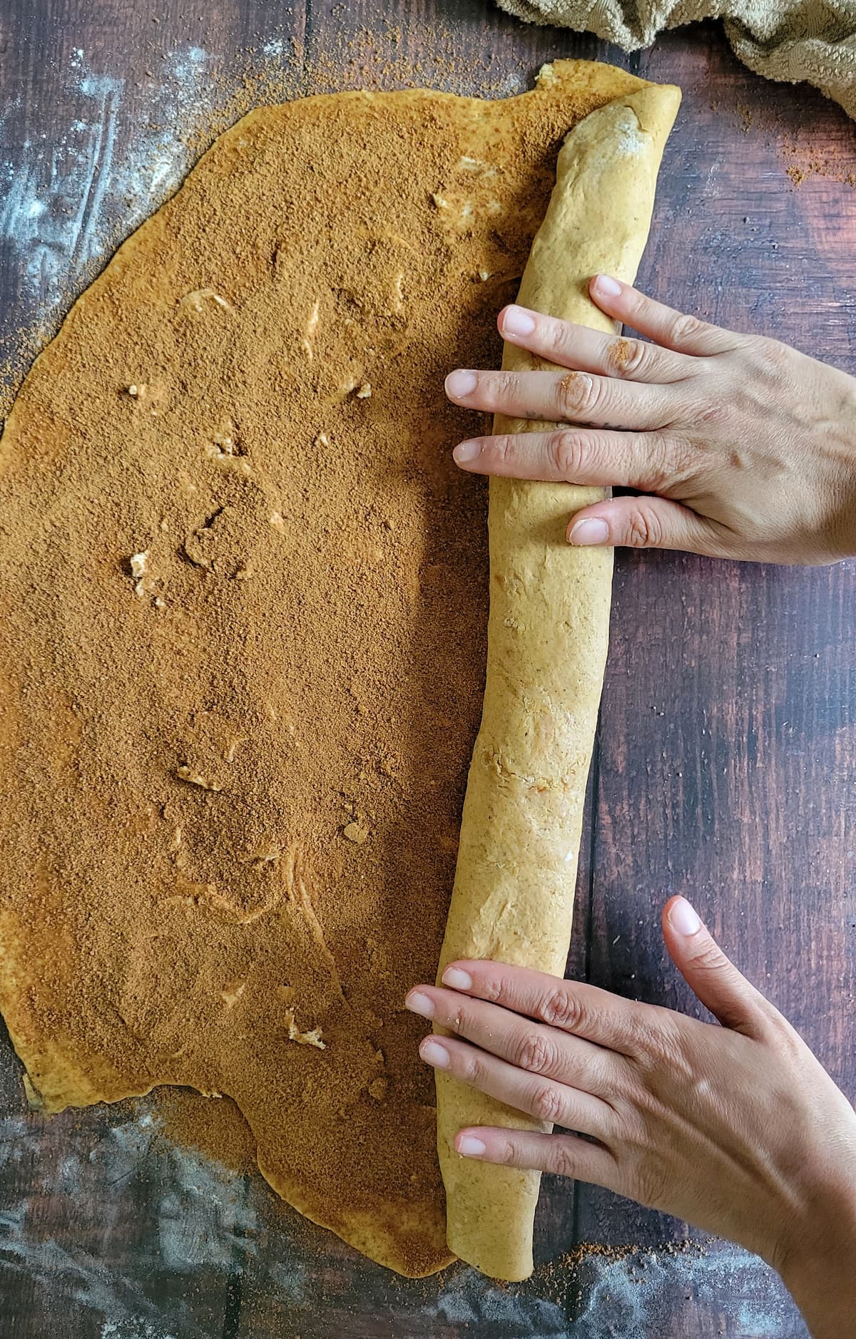 hands rolling orange dough topped with cinnamon into a tight log