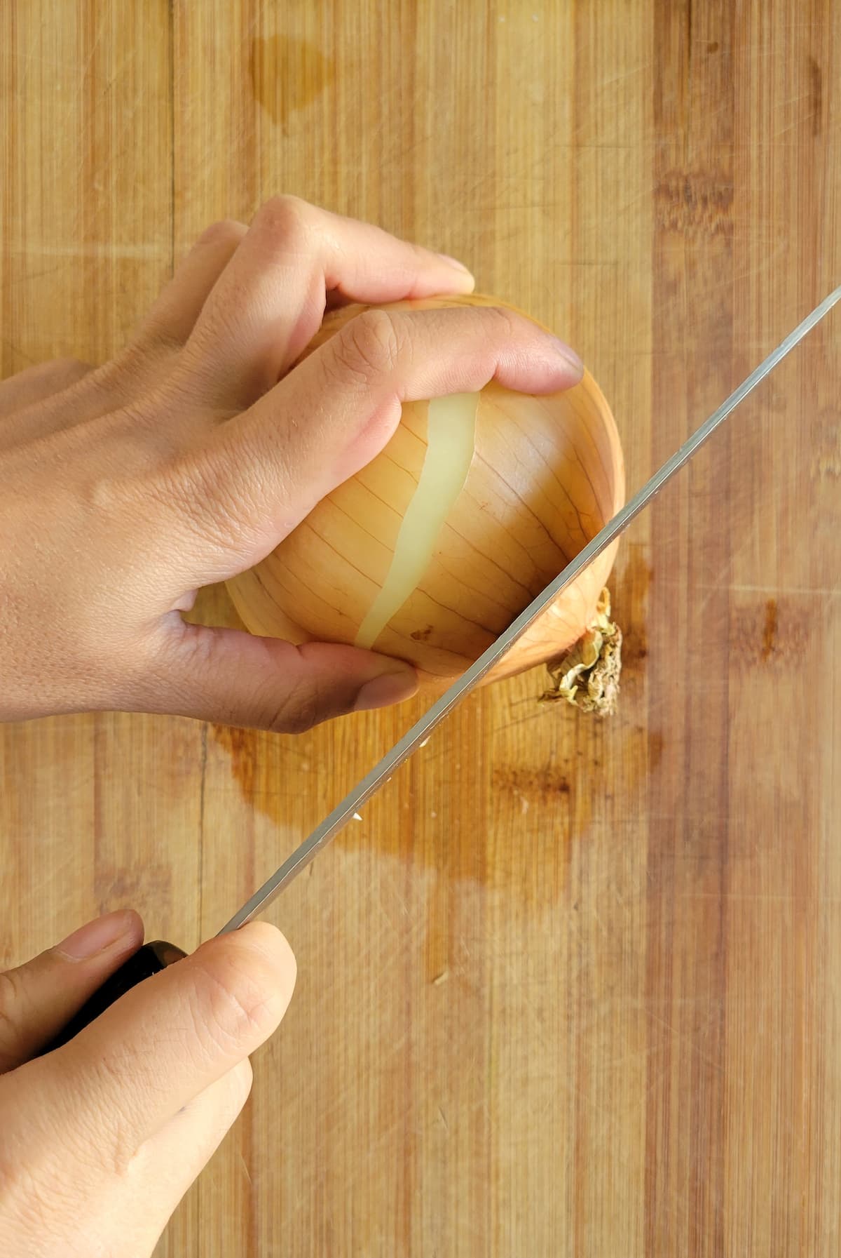 hands with a knife slicing the end off an onion
