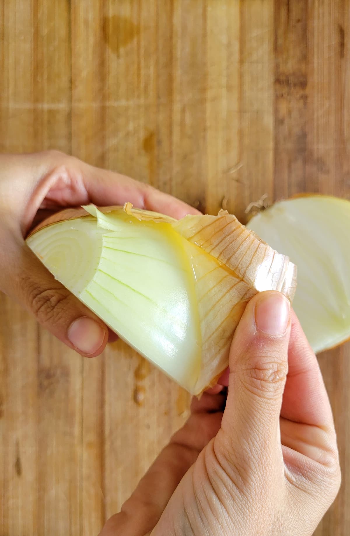 hands peeling the skin off a whole raw white onion
