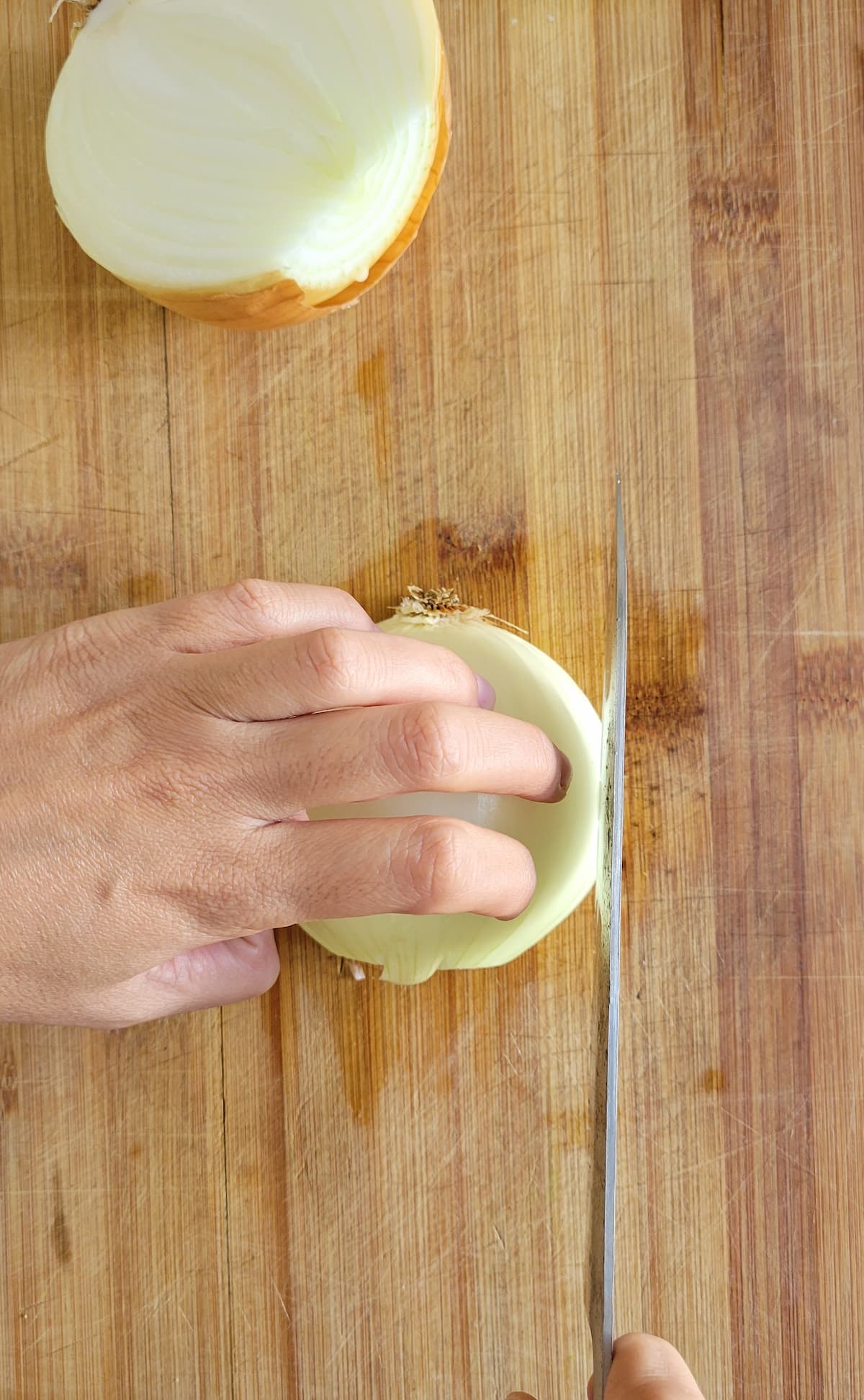 hands with a knife slicing a raw white onion