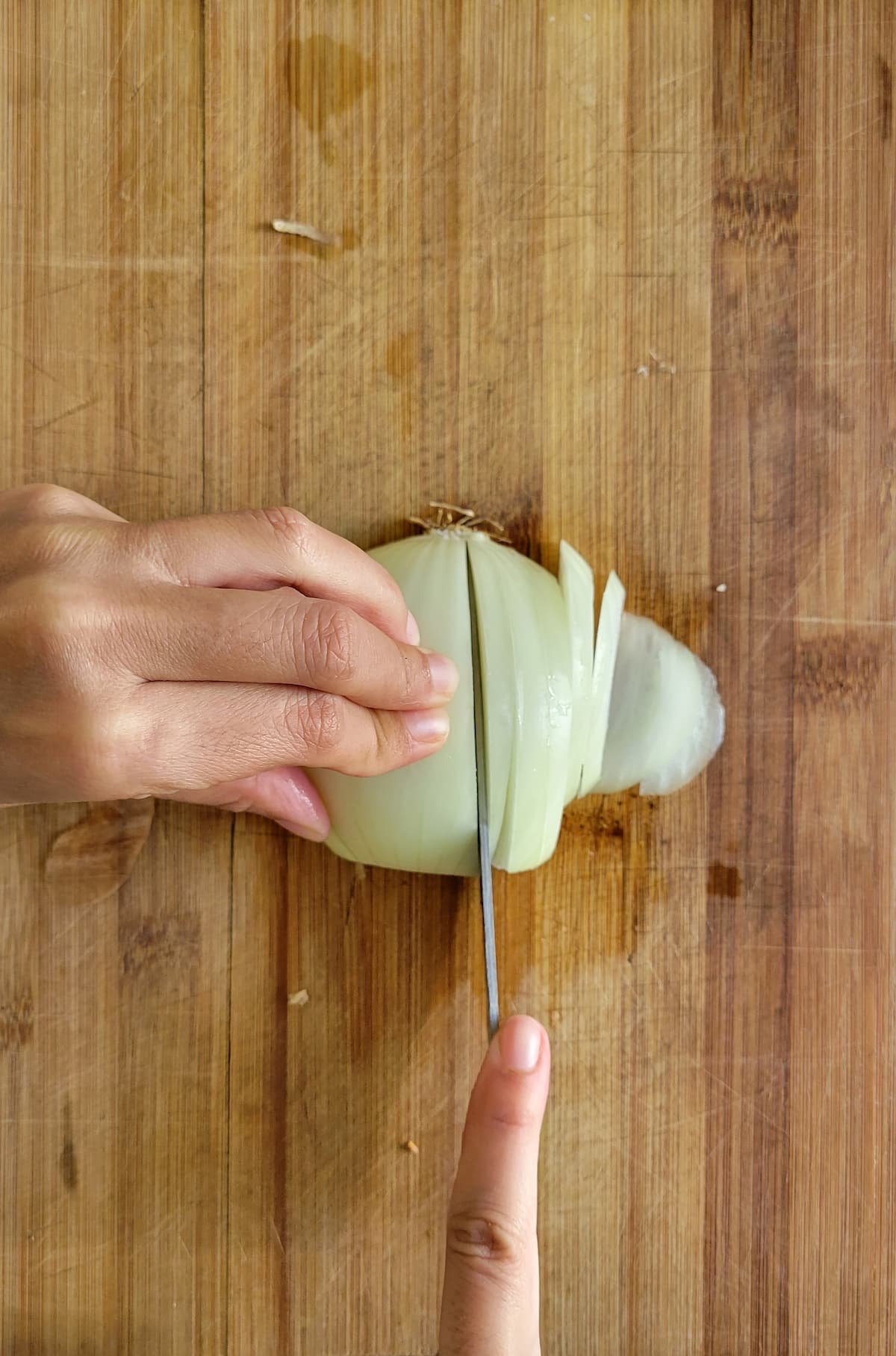 hand with a knife slicing a white onion on a cutting board