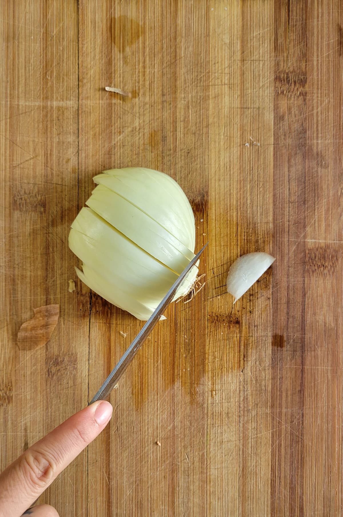 hand with a knife slicing a white onion on a cutting board