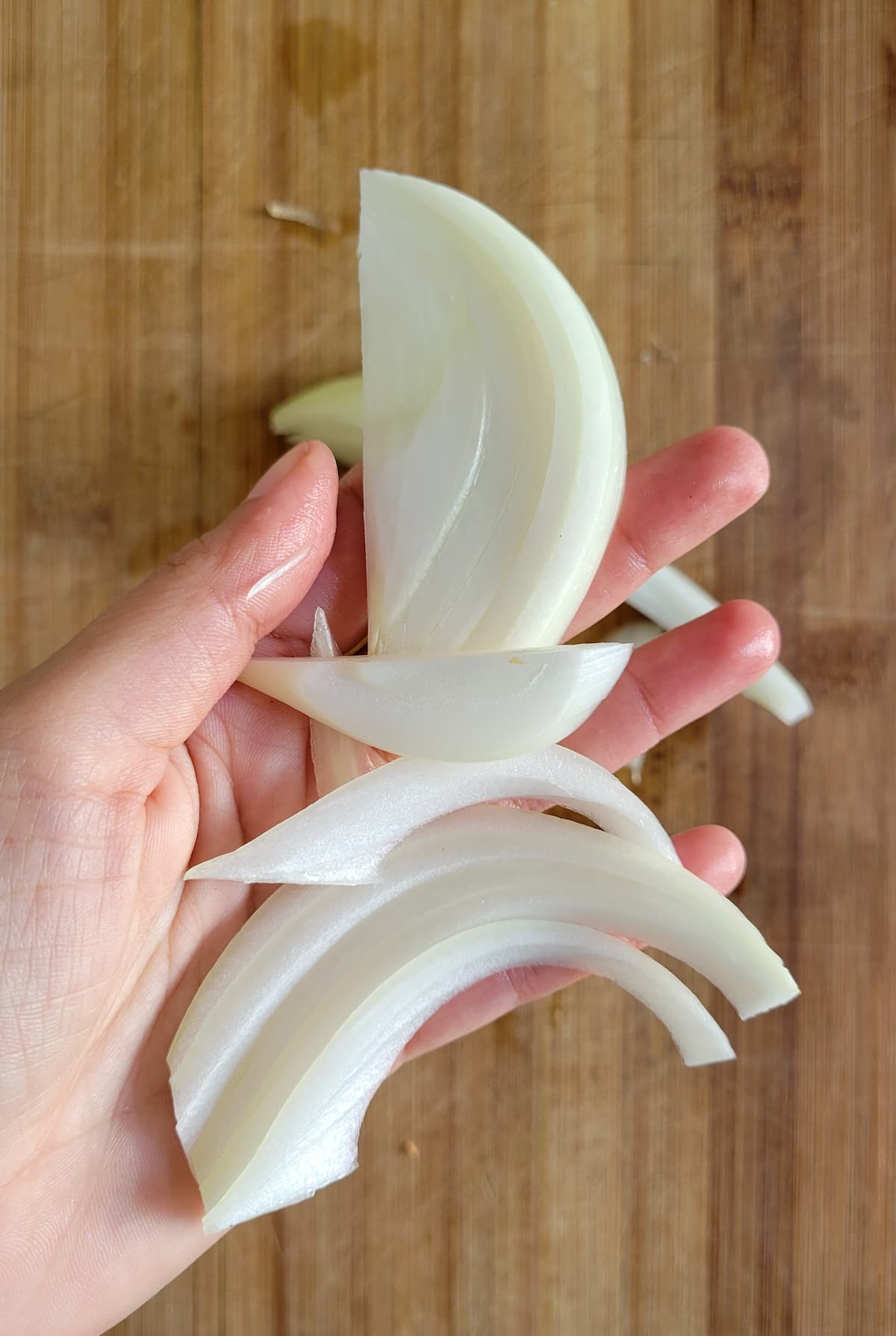 hand holding slices of raw white onion over a cutting board