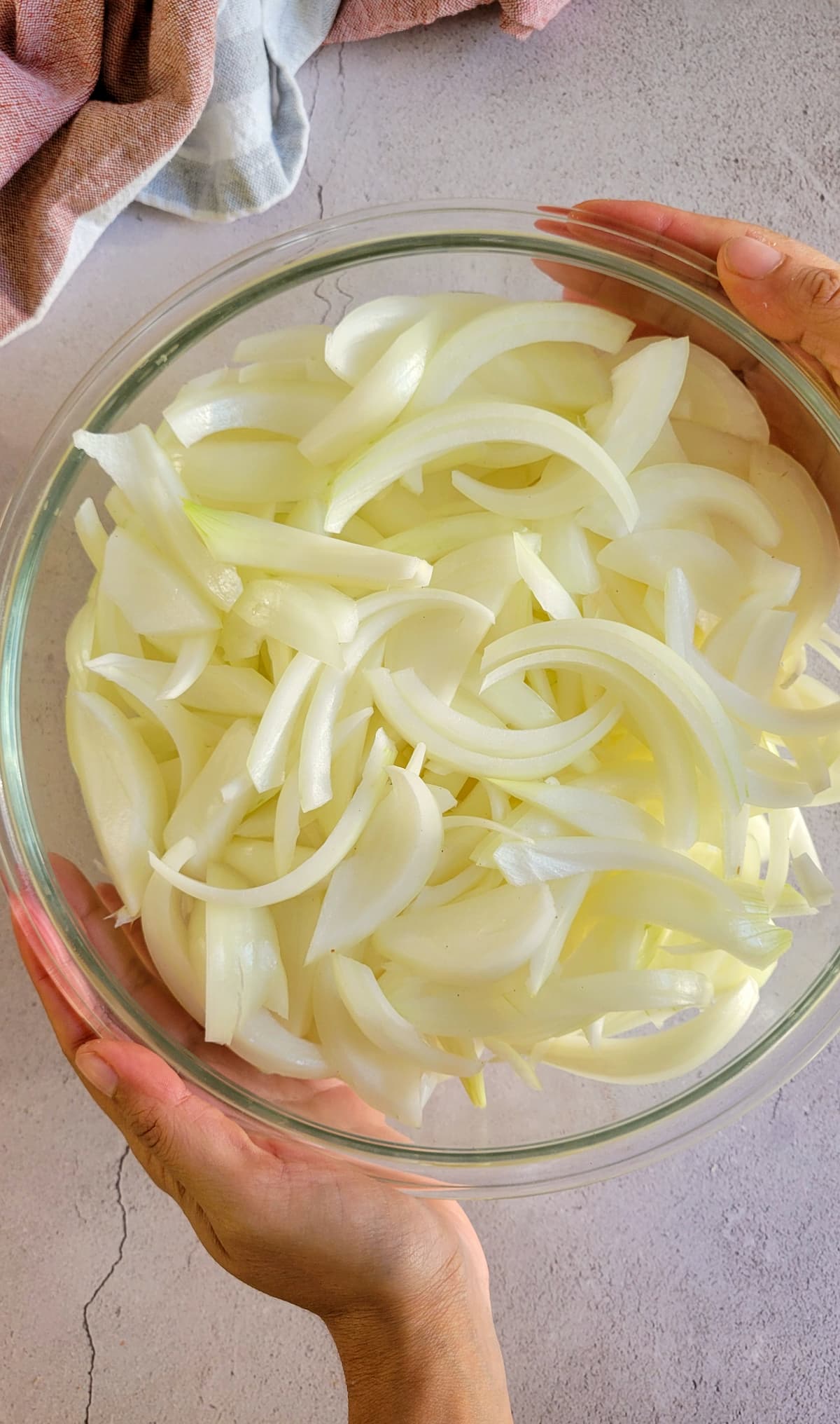 hands holding a bowl of sliced white onions