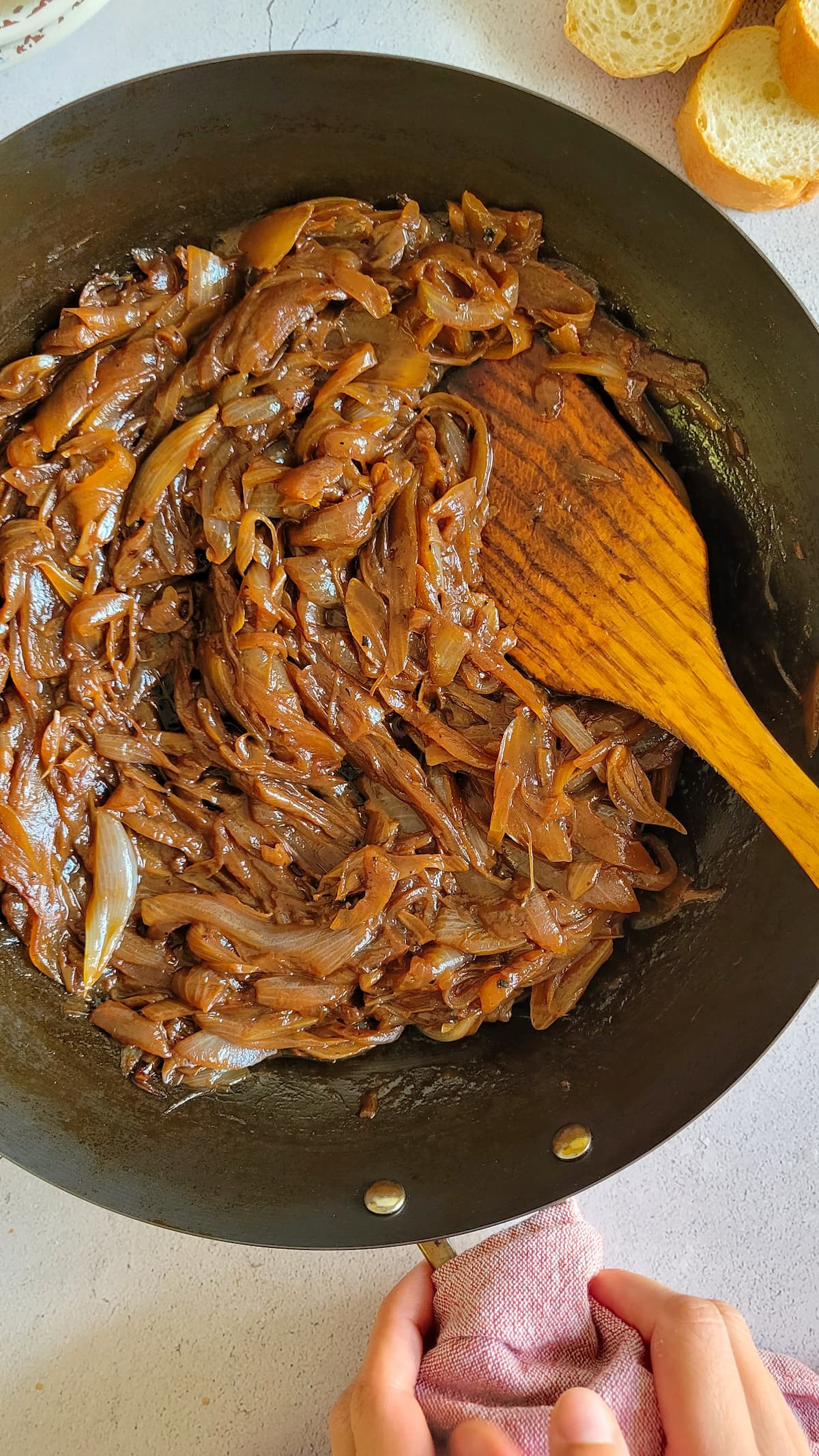 hands holding a wok of caramelised onions, wooden spatula in the skillet