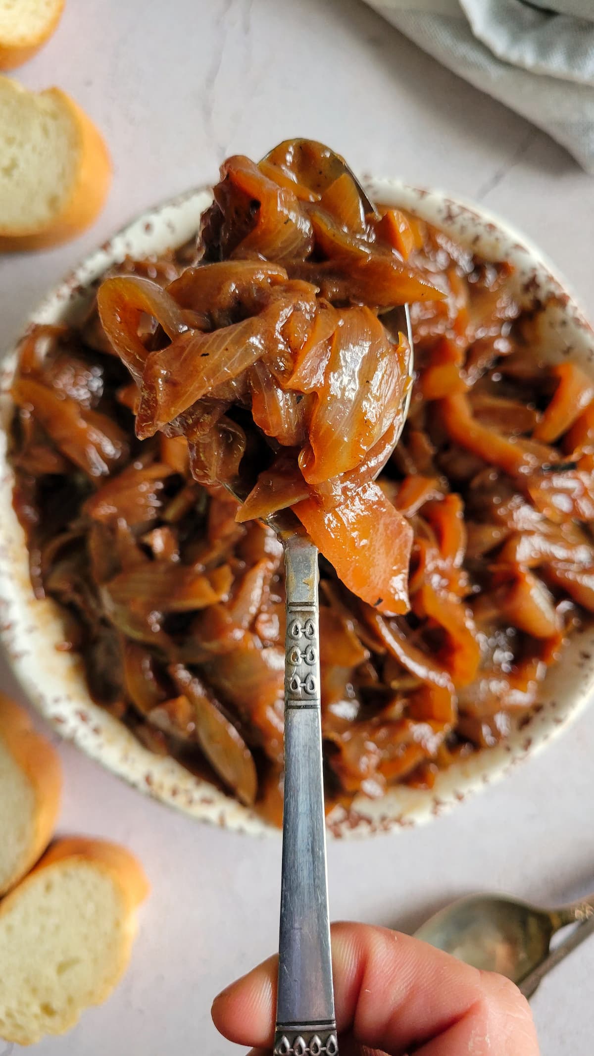 hand holding a spoonful of caramelized onions over a bowl of the rest of it, slices of bread on the side