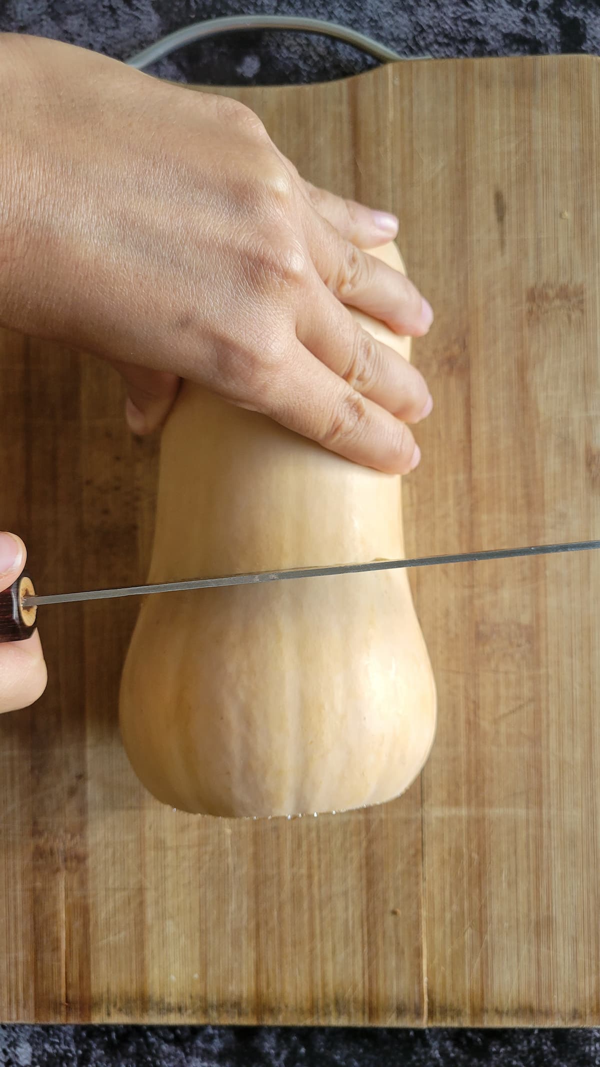hand with a knife cutting a butternut squash in half on a cutting board