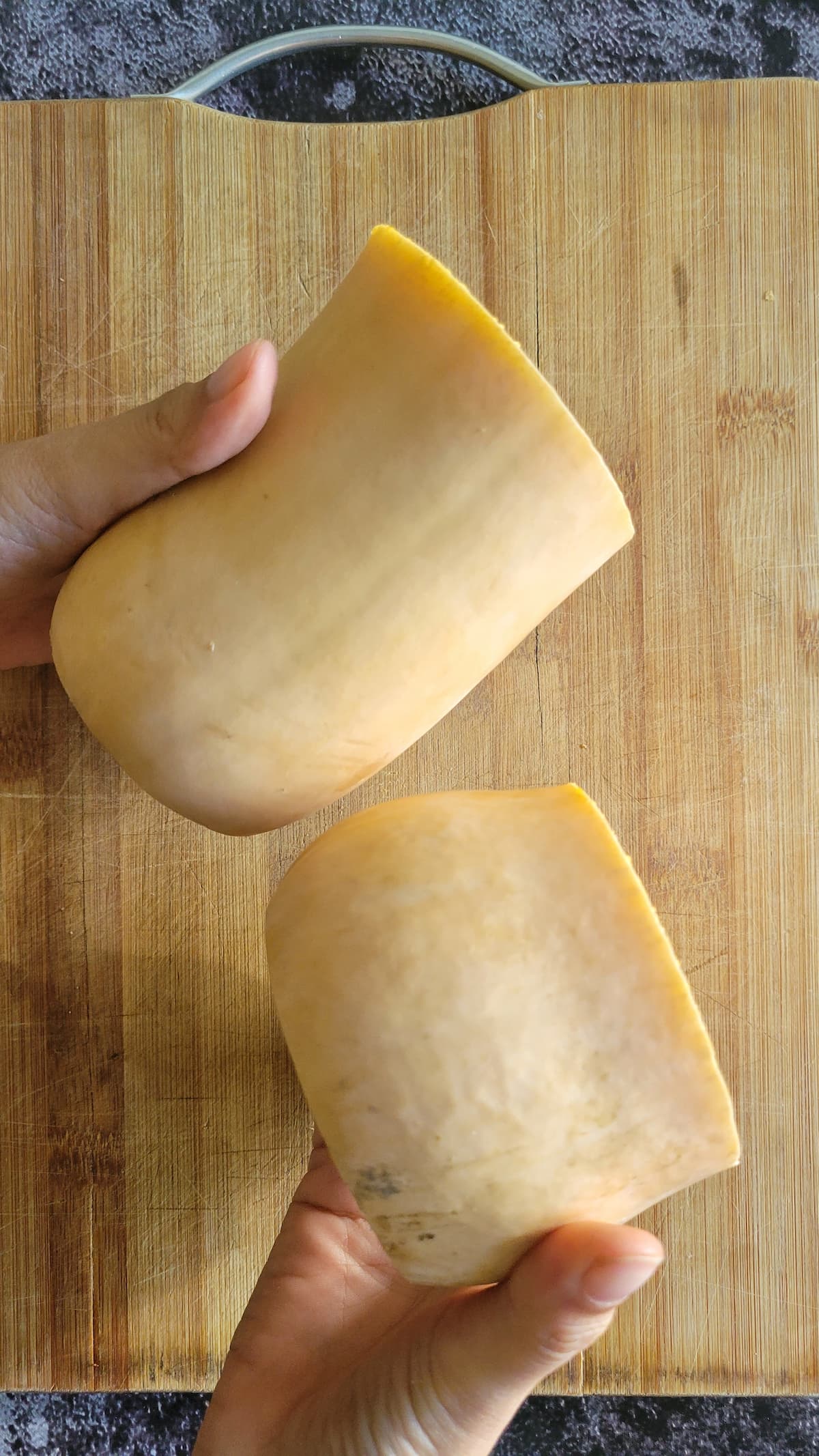 hands holding two butternut squash halves over a cutting board