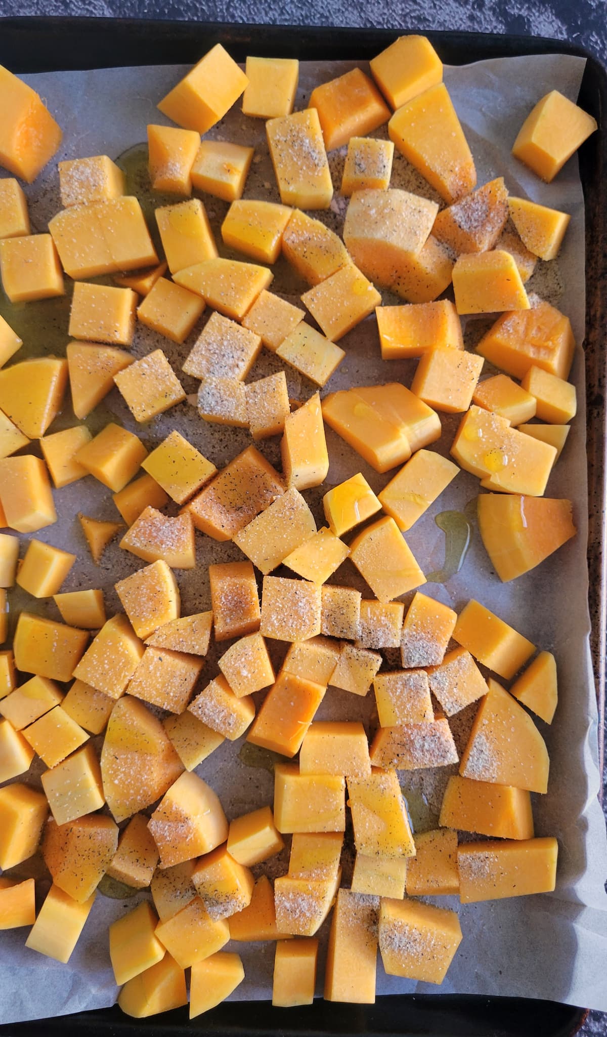 cubed butternut squash on a parchment lined baking sheet seasoned with salt and pepper