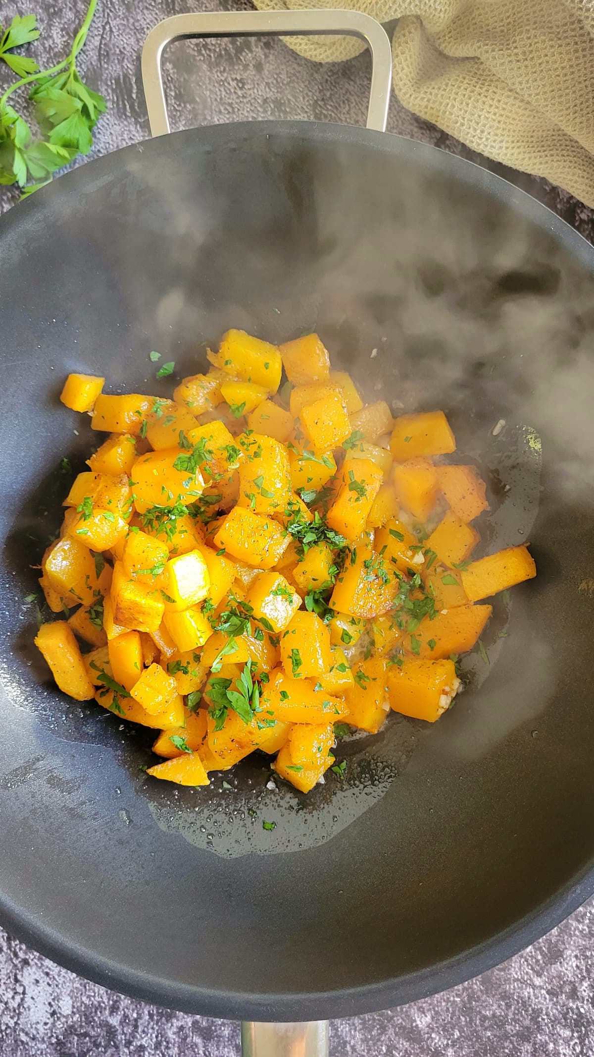cubed butternut squash cooking in a skillet with chopped parsley