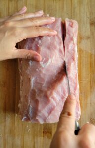 hand with a knife cutting a pork tenderloin roast down one side