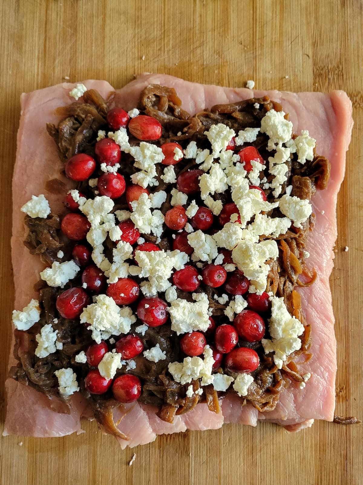 fresh cranberries, crumbled goat cheese and caramelized onions on a piece of flattened out pork tenderloin on a cutting board