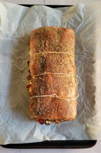 raw stuffed pork tenderloin wrapped in 3 pieces of twine on a parchment lined baking sheet
