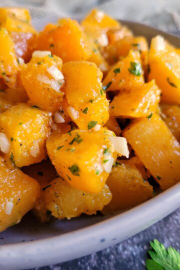 butternut squash cubes in a bowl seasoned with garlic and parsley