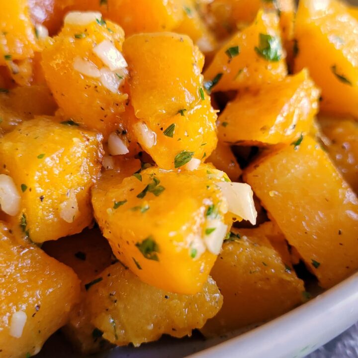 butternut squash cubes in a bowl seasoned with garlic and parsley