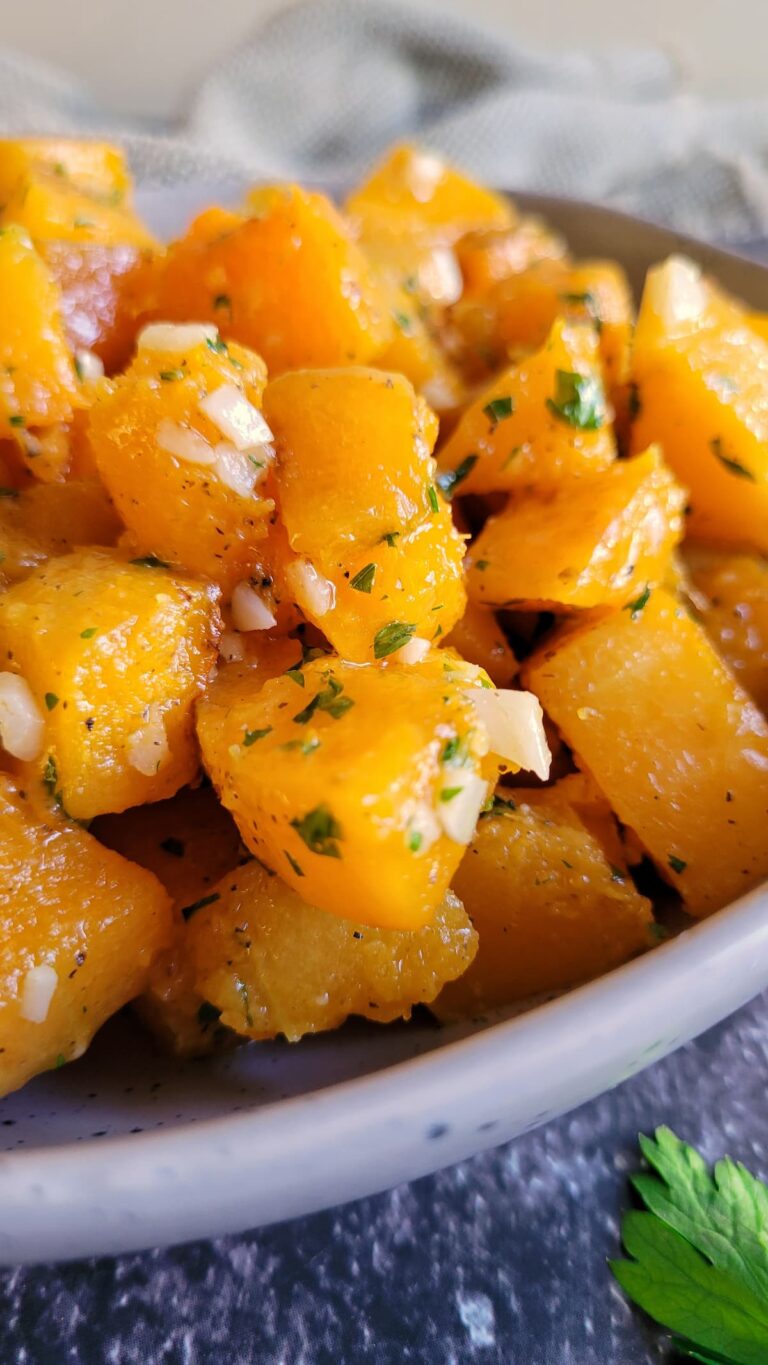 butternut squash cubes in a bowl seasoned with garlic and parsley