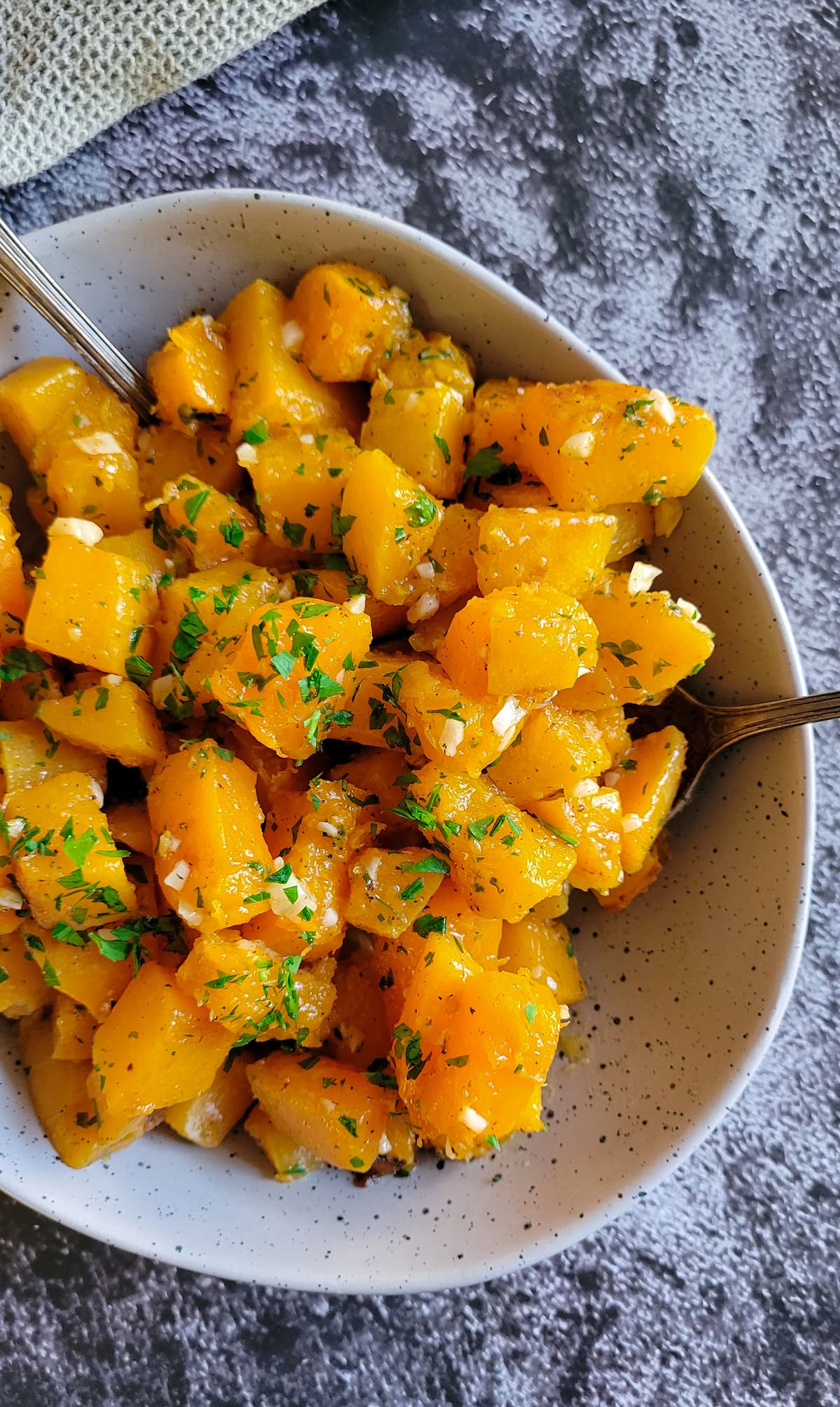 roasted butternut squash with chopped parsley and minced garlic in a bowl with 2 spoons