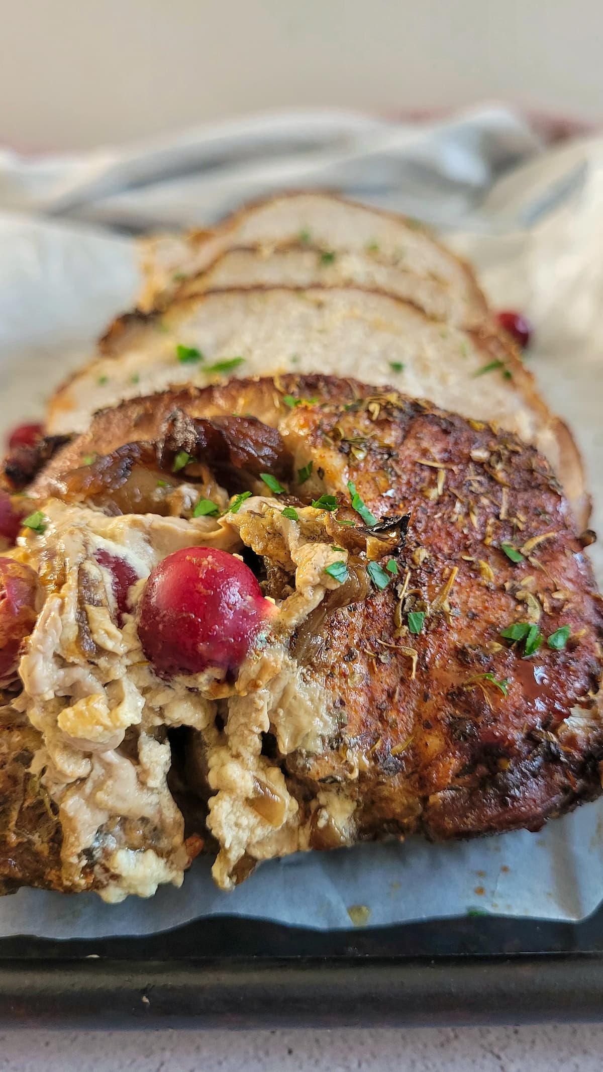slices of stuffed pork tenderloin on a parchment lined baking sheet with fresh cranberries and parsley