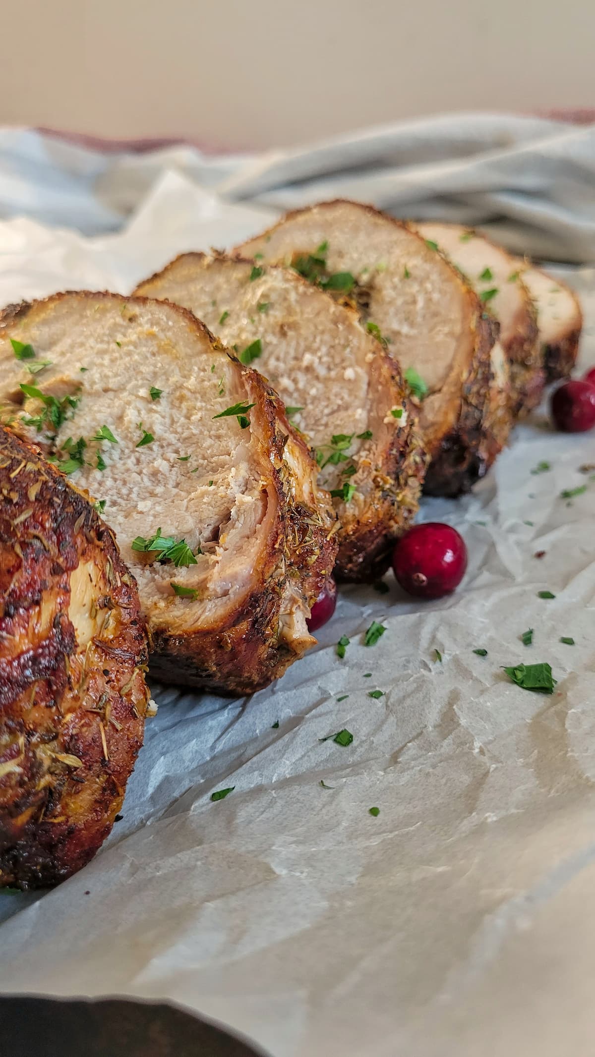 slices of pork tenderloin garnished with fresh parsley and cranberries on a parchment lined baking sheet