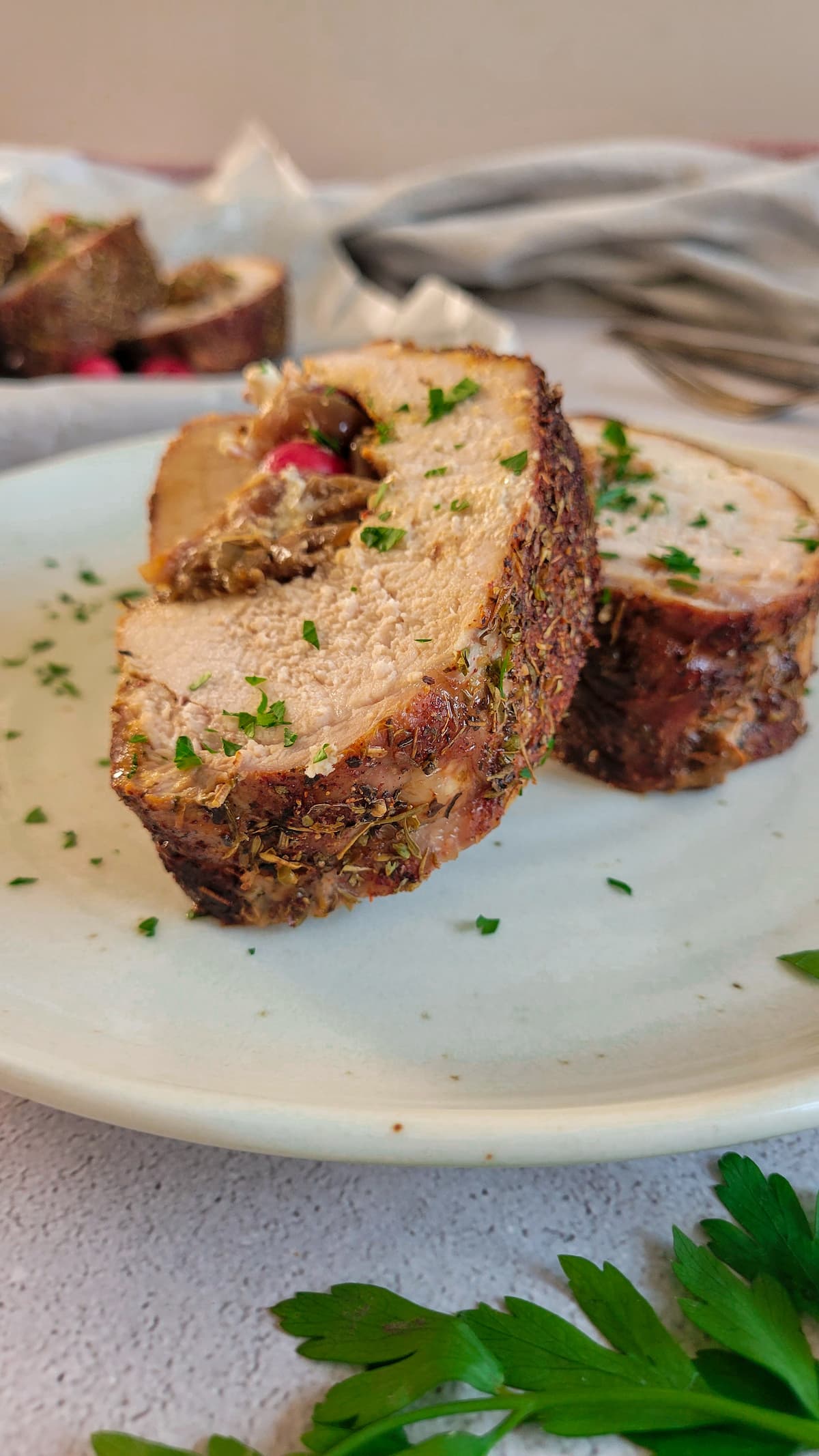 two slices of stuffed pork tenderloin on a plate, more in the background