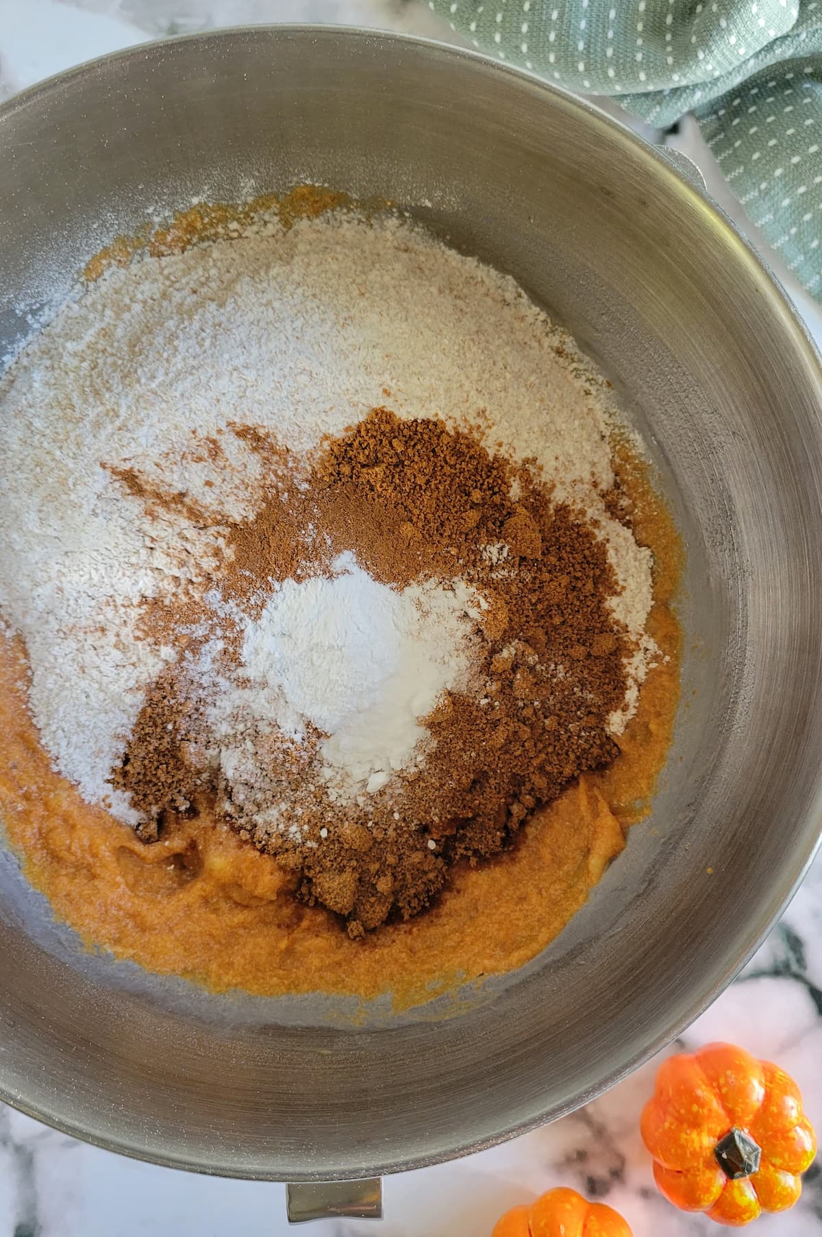 flour, sugar and spices on top of an orange batter in a bowl
