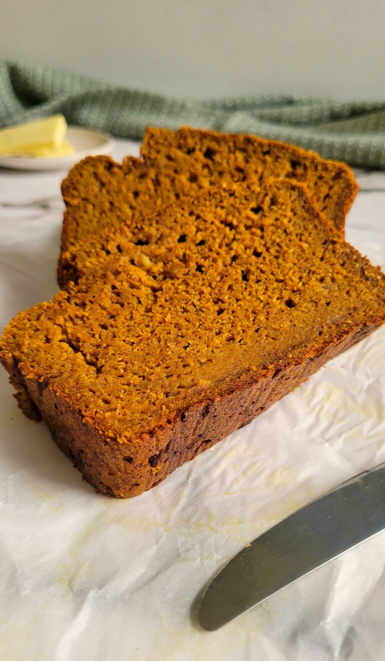 slices of banana bread on a piece of parchment paper, butter in the background, knife in the front