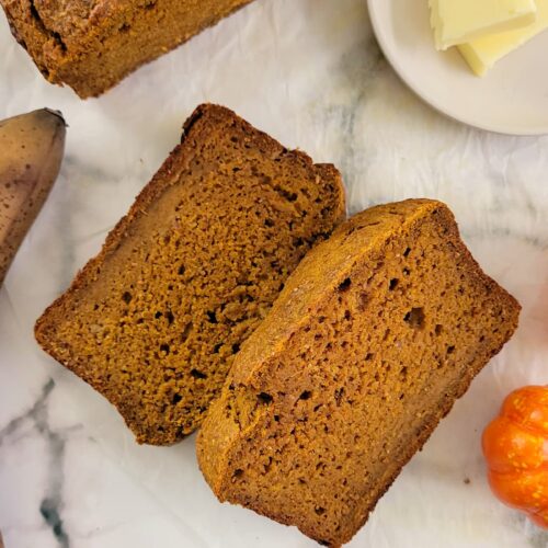 two slices of banana bread next to a whole half loaf and plate of butter