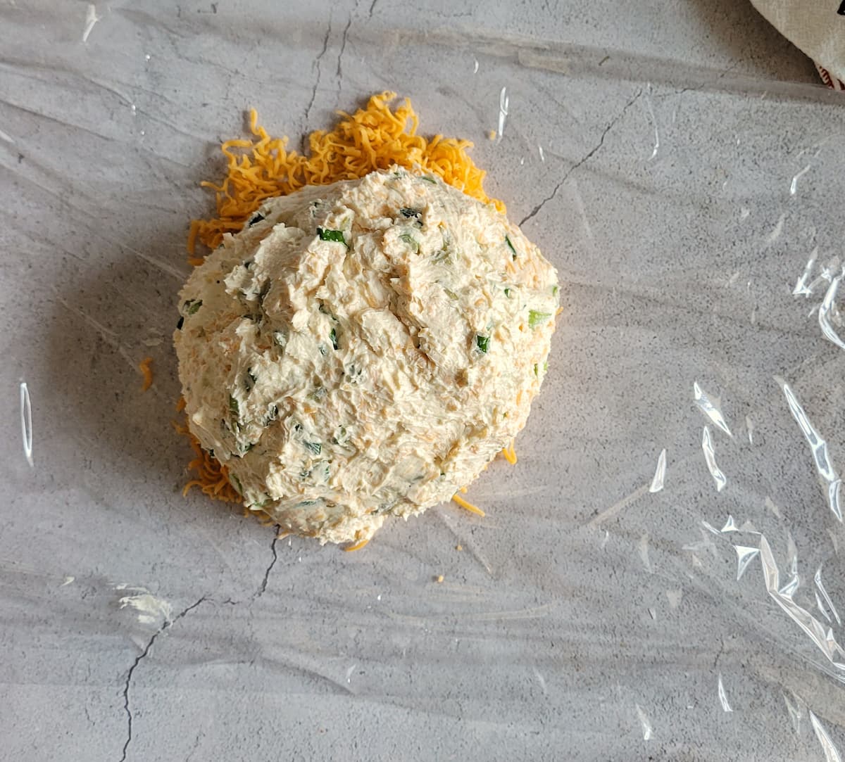 cheese ball on a pile of finely grated cheddar cheese on a piece of saran wrap