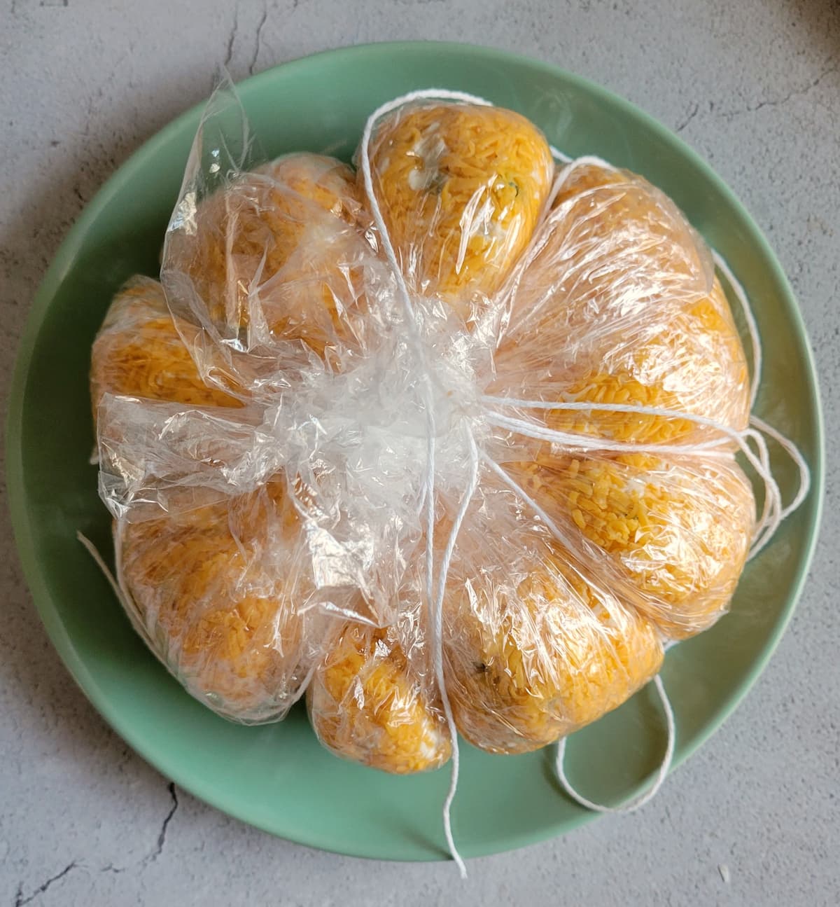 pumpkin shaped cheese ball wrapped in saran wrap and tied in string on a plate