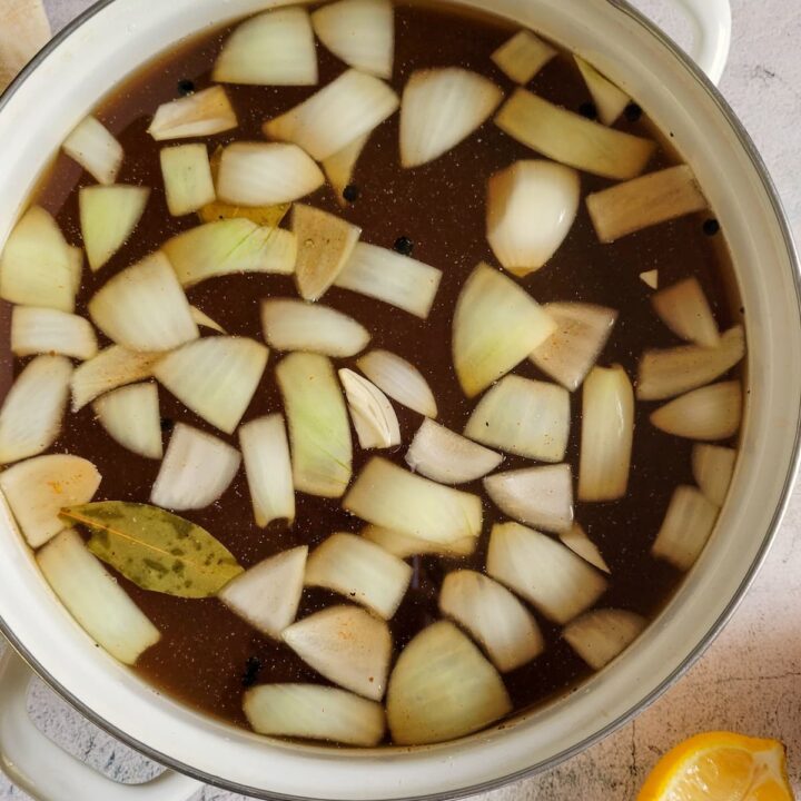 pot of stock with chopped onions and a bay leaf